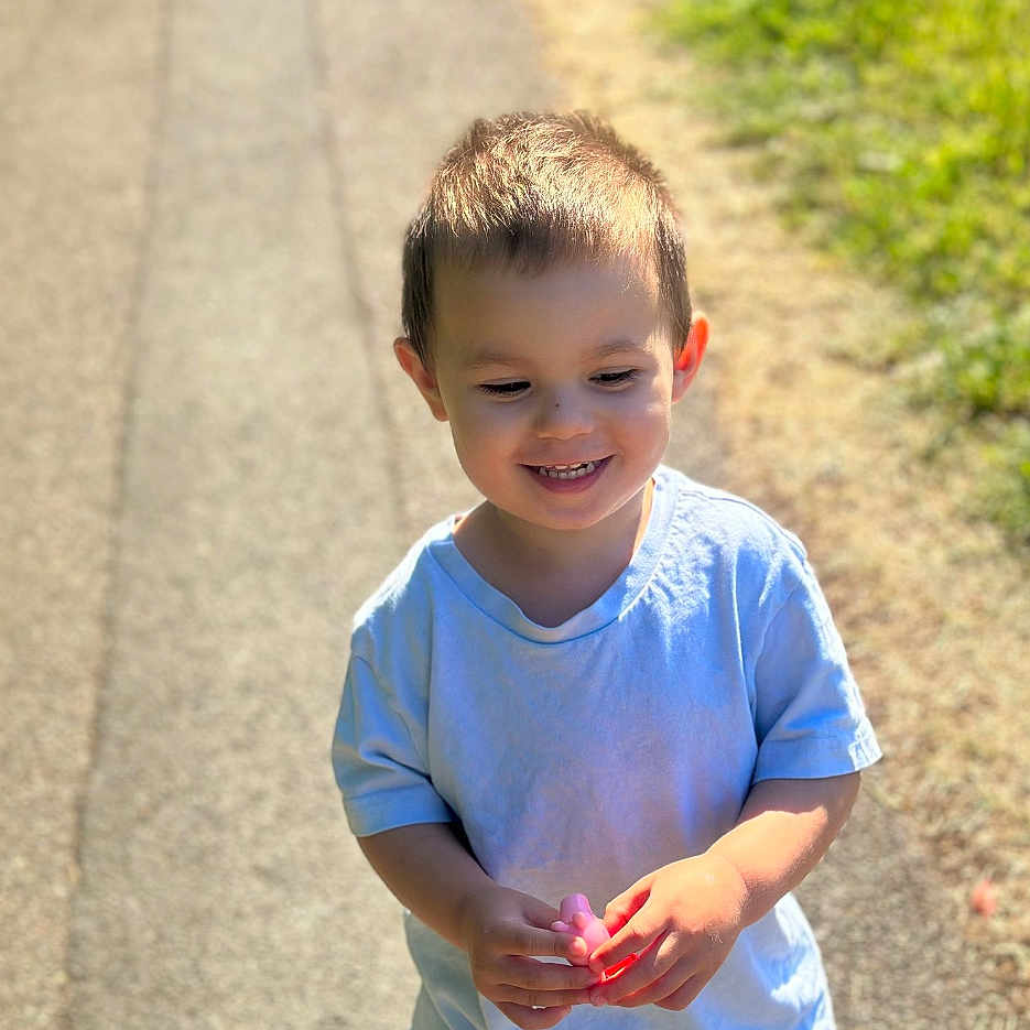 Liam joined the competition — help win amazing prizes! boy, casual_clothing, child, cute, daytime, grass, happy, holding, nature, outdoor, path, person, playing, portrait, short_hair, smiling, sunlight, toddler, toy, young