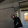 Choupette participe au concours pour gagner de l'argent avec cette photo : animal, building, calico_cat, calm, casual_clothing, cat, door, evening, glasses, headwear, hoodie, light, outdoor, person, pet, playful, posing, shoulders, wall, window