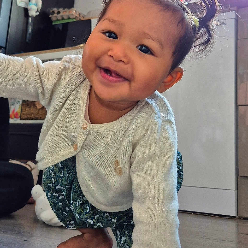 Kalyanne a rejoint le concours — aidez-le/la à gagner de superbes lots ! toddler, child, smiling, crawling, indoor, kitchen, wooden_floor, pigtails, hair_ties, sweater, pants, barefoot, happy, cute, person, baby, young_child, home, floor, playful