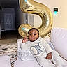 baby, child, smiling, couch, balloon, number_five, indoor, cozy, plush, white, happy, infant, clothing, relaxed, portrait, home, decor, toy, cute, person