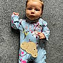 baby, infant, child, onesie, blue_clothing, floral_pattern, bird_design, wooden_sign, 3_months, hair_bow, curious_expression, lying_down, carpet, soft_texture, cute, adorable, small_hands, indoor, portrait, closeup