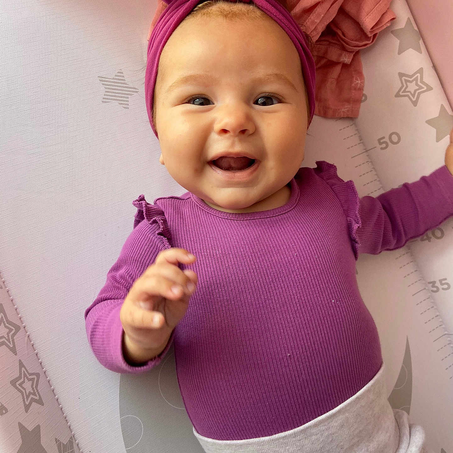 Romi-Dalton is registered to the contest to win money with this photo: apparel, baby, child, closeup, cute, expression, face, hand, happy, headband, indoors, infant, lying_down, person, play_mat, purple_clothing, skin, smiling, stars, toddler