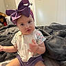 baby, child, infant, portrait, sitting, indoors, blanket, bed, bow, hair_accessory, purple, floral_clothing, bib, shorts, toy, home, door, laundry_basket, facial_expression, photography