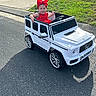 Camila is registered to the contest to win money with this photo: baby, child, toddler, smiling, red_bow, red_dress, toy_car, luxury_car, white_vehicle, ride_on_car, outdoor, driveway, grass, asphalt, sunlight, portrait, happy, vehicle, front_grille, mercedes_style