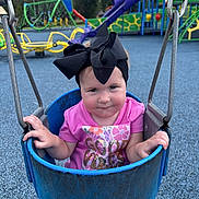 Camila joined the competition — help win amazing prizes! baby, child, toddler, playground, swing, swing_set, portrait, face, bow, hair_bow, pink_shirt, smiling, outdoor, playground_equipment, slide, climbing_frame, playground_surface, daylight, seated, colorful