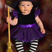 Amelia Rose joined the competition — help win amazing prizes! baby, child, costume, witch_hat, broomstick, striped_tights, black_shoes, purple_dress, leather_chair, portrait, cute, indoor, holiday, halloween, festive, sitting, young_child, face, smiling, playful