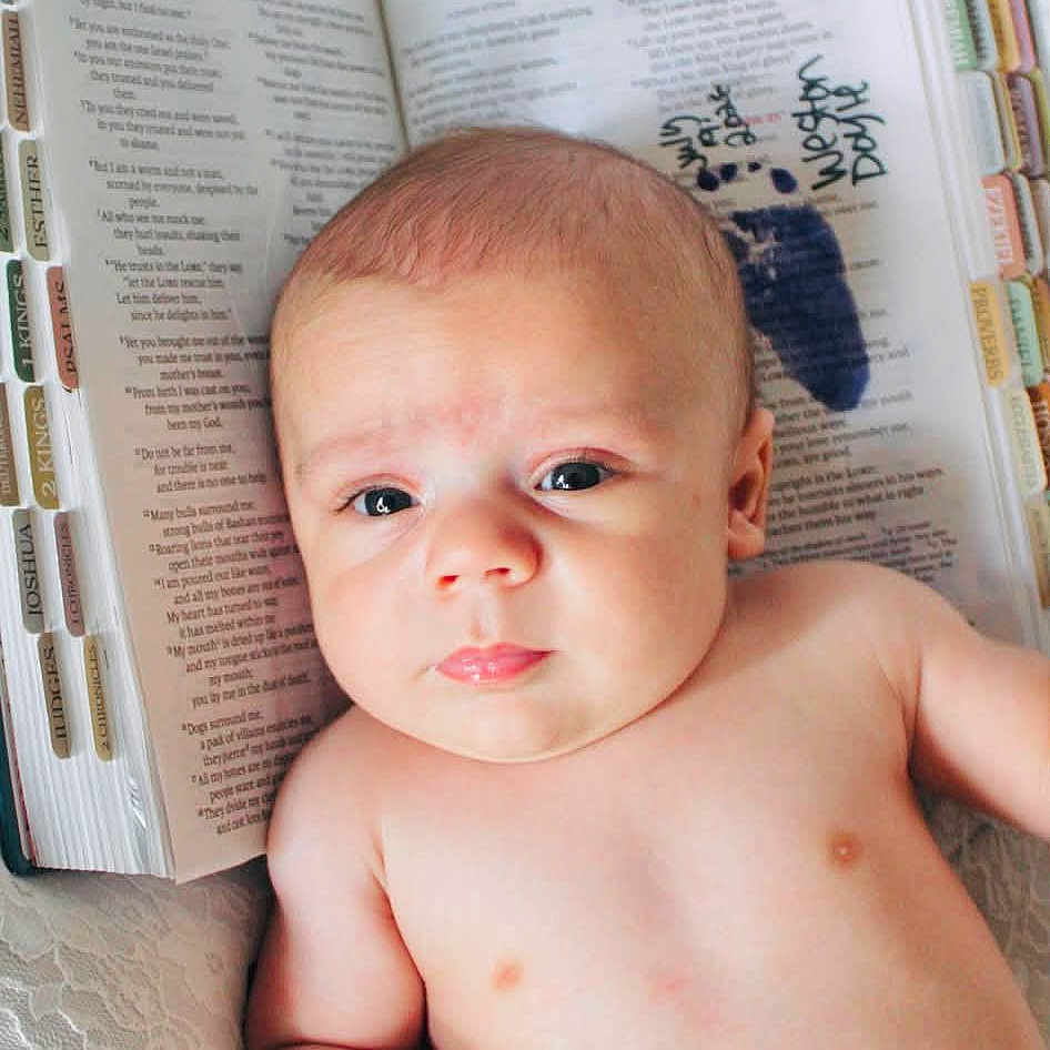 Weston Huffman joined the competition — help win amazing prizes! baby, infant, shirtless, face, eyes, expression, bible, book, pages, text, lace, background, skin, human, newborn, lying_down, indoors, closeup, portrait, serious