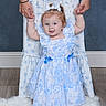 baby, child, dress, blue_and_white, holding_hands, adult, floor, rug, hair_bow, pigtails, smiling, indoor, portrait, person, standing, happy, cute, flooring, patterned_clothing, family
