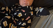 Colton is registered to the contest to win money with this photo: baby, infant, onesie, bed, blanket, sleepwear, face, person, cute, expression, newborn, child, lying_down, patterned_clothing, soft_fabric, indoors, portrait, young_child, awake, curious