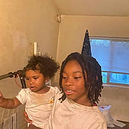 Saniyah is registered to the contest to win money with this photo: african_american, casual_clothing, child, curly_hair, curtains, family, holding, home, indoor, natural_light, person, room, shirt, siblings, smile, standing, toddler, window, young_child
