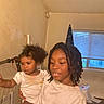 african_american, casual_clothing, child, curly_hair, curtains, family, holding, home, indoor, natural_light, person, room, shirt, siblings, smile, standing, toddler, window, young_child