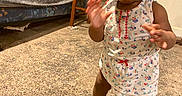 Saniyah joined the competition — help win amazing prizes! barefoot, blanket, bottle, carpet, child, clothing, curious, curly_hair, cute, floor, indoor, lollipop, person, plaid_couch, room, snack, standing, toddler, wall, wooden_table