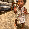 barefoot, blanket, bottle, carpet, child, clothing, curious, curly_hair, cute, floor, indoor, lollipop, person, plaid_couch, room, snack, standing, toddler, wall, wooden_table