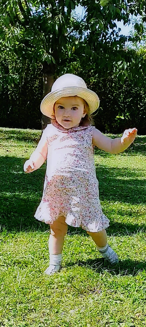 Emma a rejoint le concours — aidez-le/la à gagner de superbes lots ! baby_toddler_clothing, botany, dress, face, finger, gesture, grass, happy, hat, headwear, leaf, leisure, nature, people_in_nature, person, photograph, plant, sleeve, summer, sun_hat