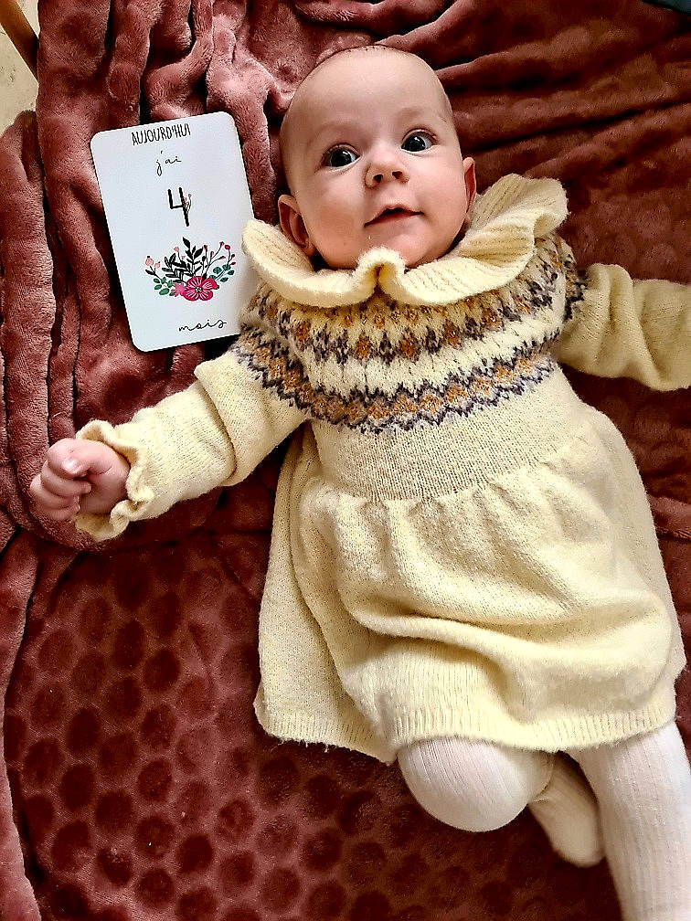 Abigaïl a rejoint le concours — aidez-le/la à gagner de superbes lots ! baby, baby_products, baby_toddler_clothing, cheek, child, dress, face, facial_expression, finger, gesture, happy, head, pattern, person, pink, sitting, skin, sleeve, smile, thumb