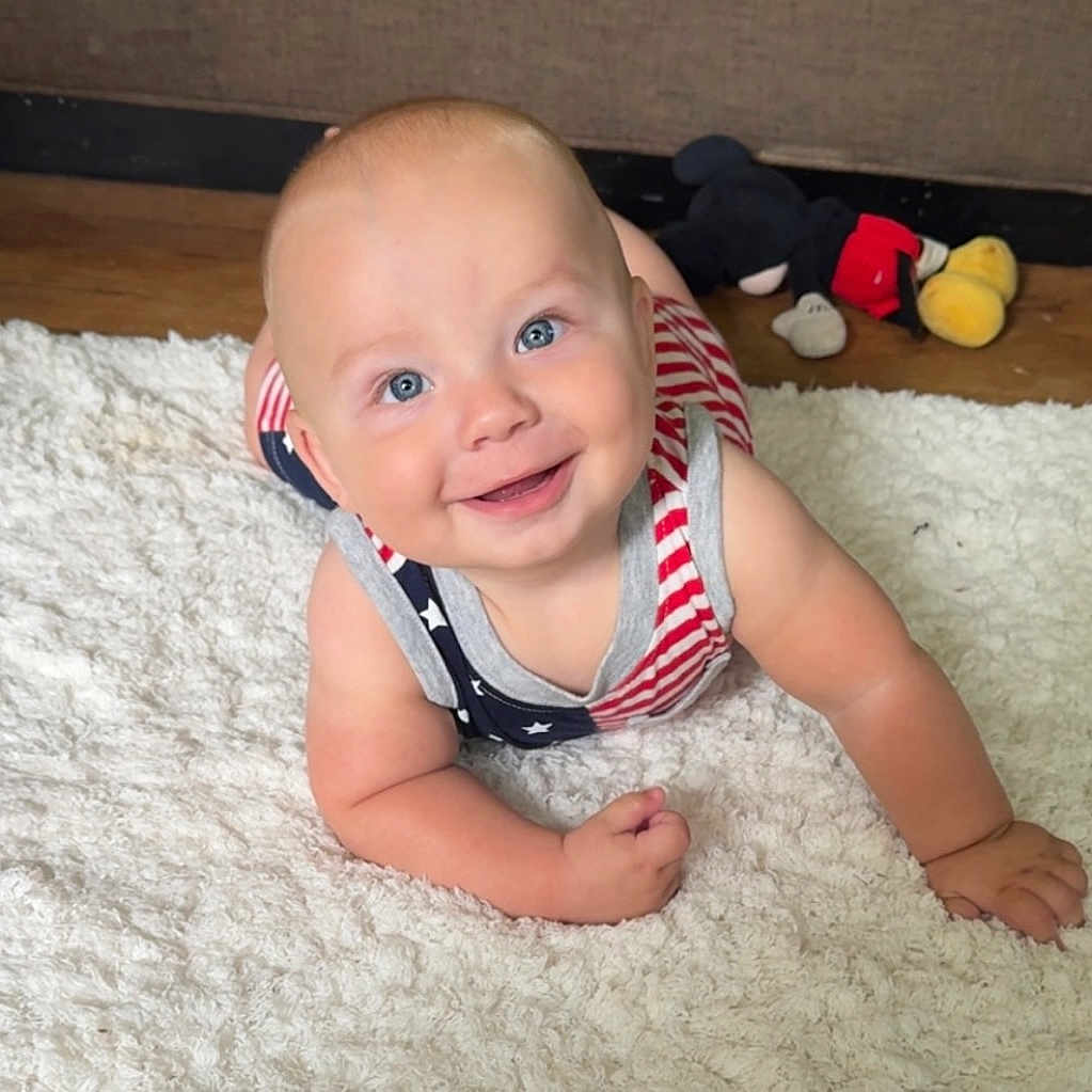 Vince joined the competition — help win amazing prizes! american_flag_pattern, baby, blue_eyes, child, clothing, crawling, cute, floor, happy, indoor, infant, mickey_mouse, patterned_outfit, person, plush_toy, rug, skin, smiling, toy, wooden_floor