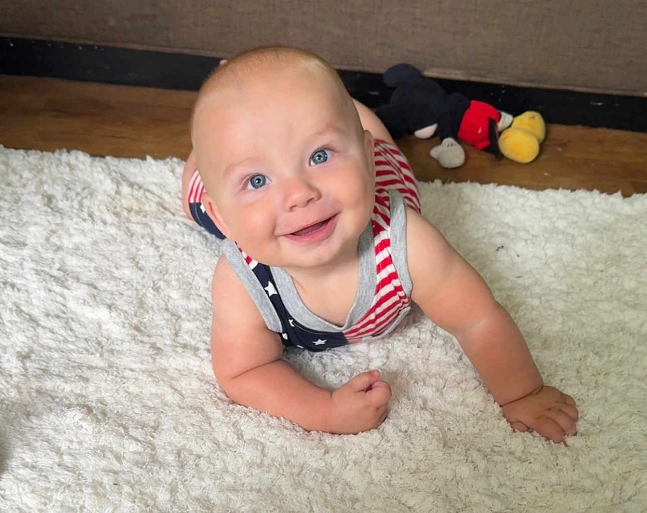 Vince joined the competition — help win amazing prizes! baby, smiling, blue_eyes, infant, crawling, rug, plush_toy, mickey_mouse, toy, floor, wooden_floor, indoor, child, cute, happy, clothing, patterned_outfit, american_flag_pattern, skin, person