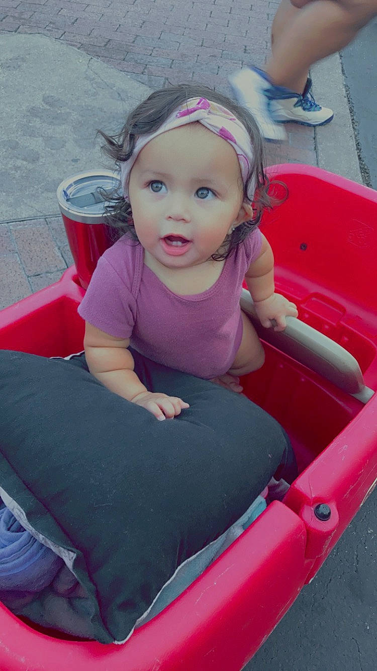 Delaney is registered to the contest to win money with this photo: automotive_exterior, baby, baby_toddler_clothing, bumper, chair, dress, face, fun, grass, hair, happy, head, human_leg, leisure, magenta, motor_vehicle, person, pink, recreation, toddler