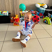 Lewen participe au concours pour gagner de l'argent avec cette photo : baby, ball, child, clothing, colorful, floor, happy, indoor, person, plastic_toys, playing, sitting, smiling, soccer_ball, socks, sportswear, tiles, toddler, toys, white_shoes