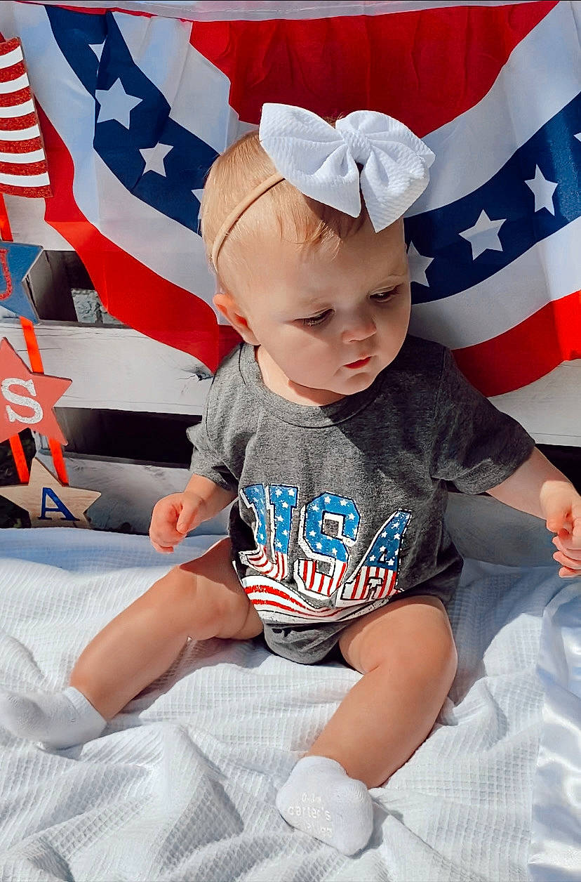 Nova joined the competition — help win amazing prizes! baby, baby_toddler_clothing, child, costume_hat, event, flag, flag_day_usa, flag_of_the_united_states, fun, happy, holiday, human_leg, person, red, sitting, sleeve, t_shirt, textile, thigh, toddler