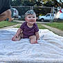 baby, child, smiling, purple_onesie, headband, bow, blanket, outdoor, grass, garden, happy, sitting, infant, cute, face, parked_car, person, foot, skin, daylight