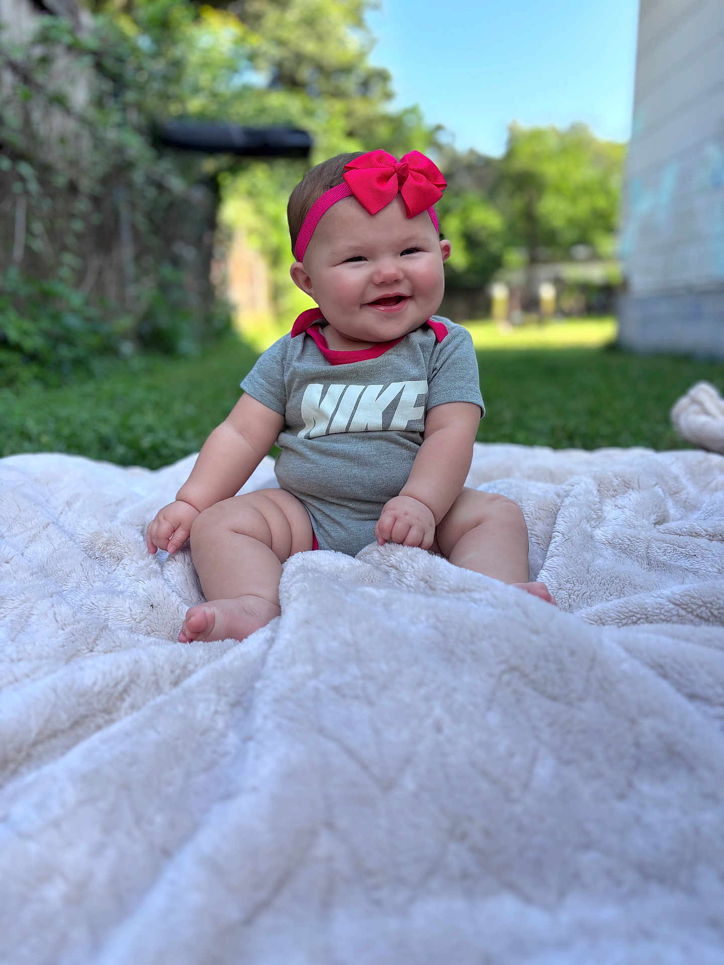 Desiree is registered to the contest to win money with this photo: baby, child, smiling, bow, headband, onesie, nike, blanket, outdoor, grass, greenery, garden, happy, cute, infant, sitting, soft_texture, portrait, daylight, nature
