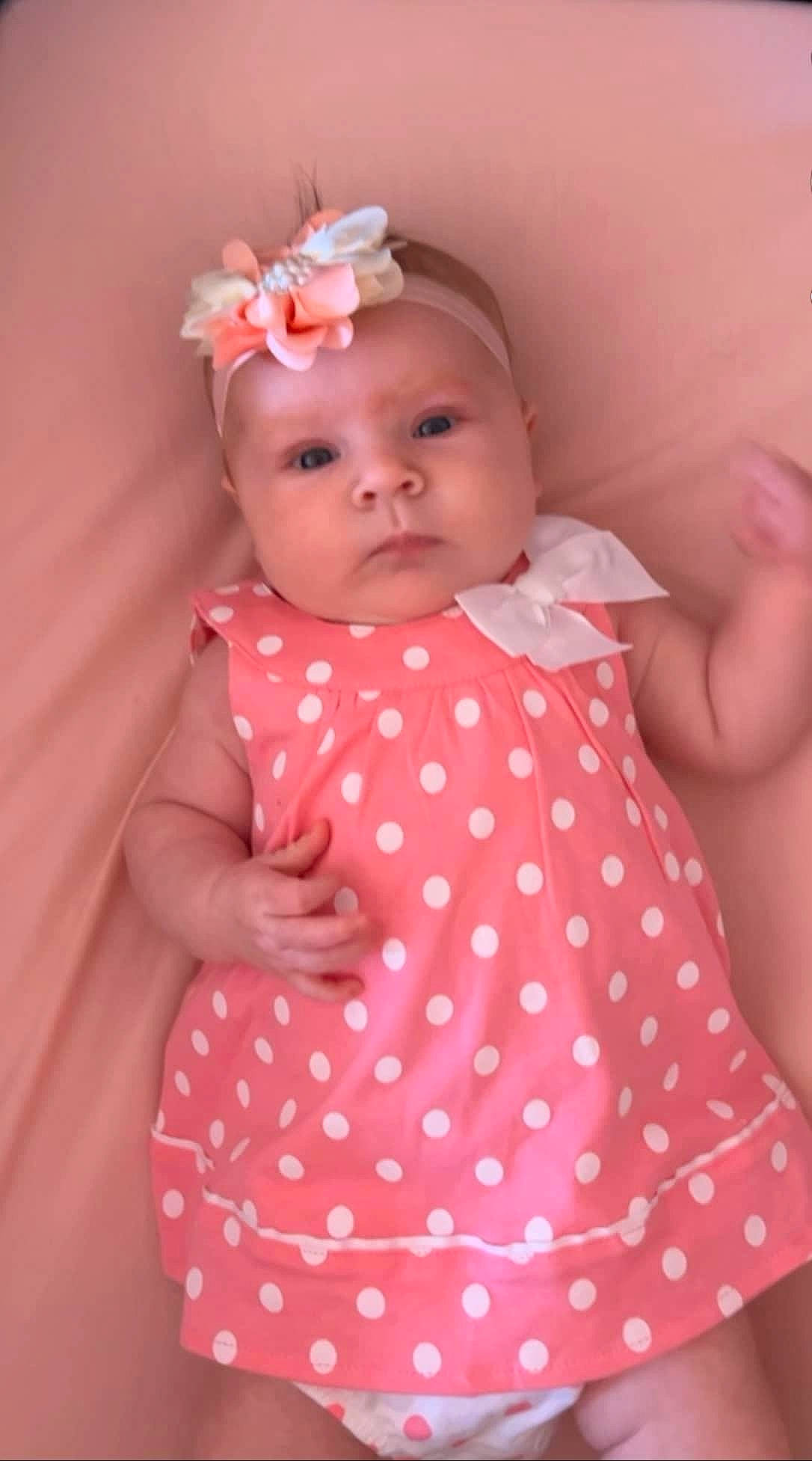 Caroline is registered to the contest to win money with this photo: arm, baby, baby_products, baby_toddler_clothing, cheek, child, dress, eye, eyelash, finger, hand, headwear, human_body, lip, neck, pattern, person, pink, skin, sleeve