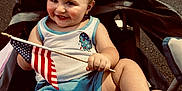 Evander joined the competition — help win amazing prizes! american_flag, barefoot, celebration, chair, child, cute, daylight, flag, fun, happy, outdoor, patriotic, person, shorts, sitting, smiling, summer, tank_top, toddler, young_child