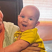 Jace is registered to the contest to win money with this photo: baby, child, smile, yellow_shirt, indoor, adult_hand, curtain, happy, person, face, arm, holding, joy, light, casual_clothing, infant, expression, cute, human, portrait