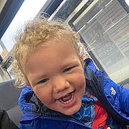 Diego joined the competition — help win amazing prizes! child, toddler, curly_hair, blue_jacket, smiling, teeth, indoor, bus_stop, window, seat, clothing, person, portrait, happy, casual, young, cute, spiderman_shirt, light, face