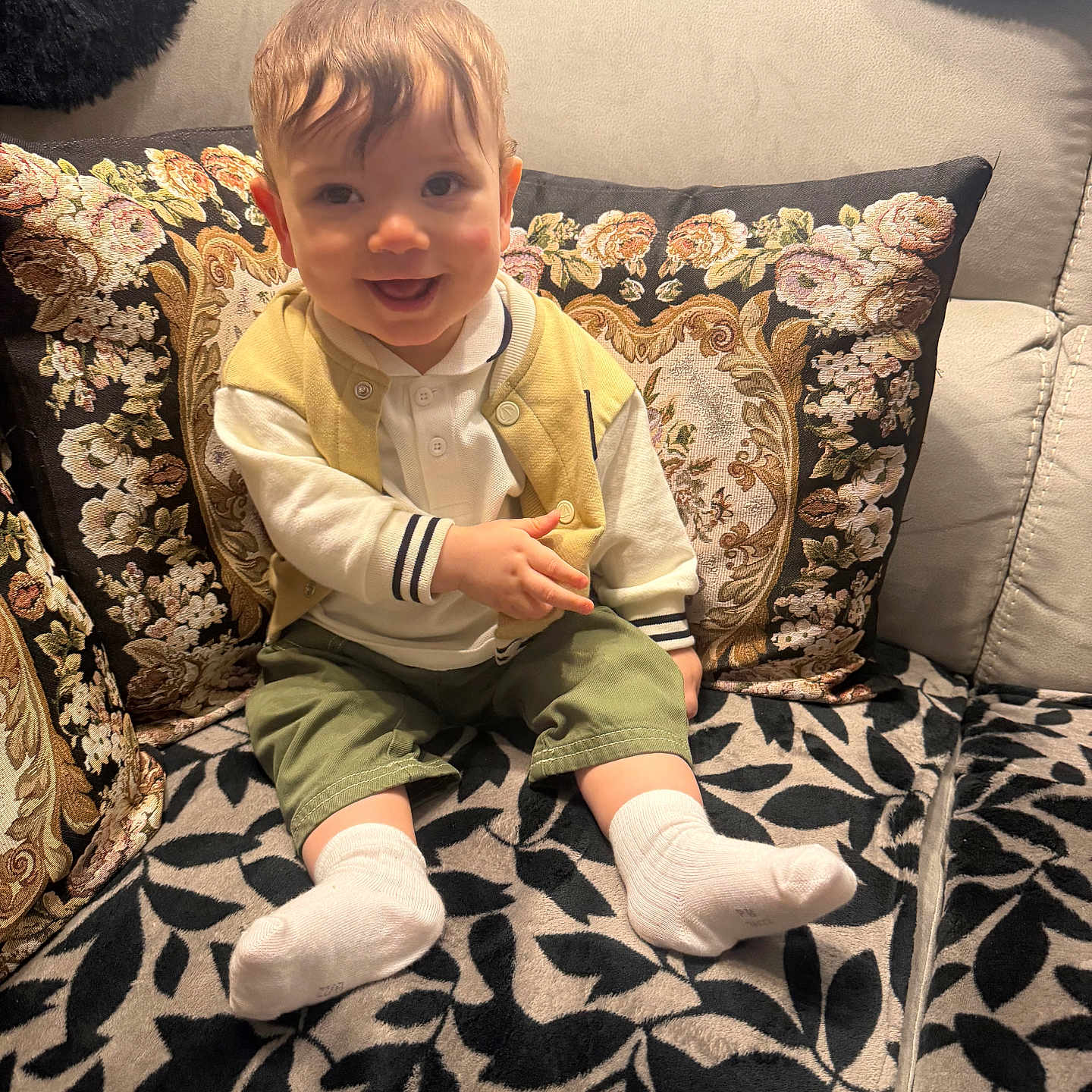 Adam participe au concours pour gagner de l'argent avec cette photo : baby, child, smiling, couch, cushion, floral_pattern, leaf_pattern, white_socks, yellow_vest, green_shorts, white_shirt, indoor, portrait, happy, seated, person, home, cozy, cute, infant