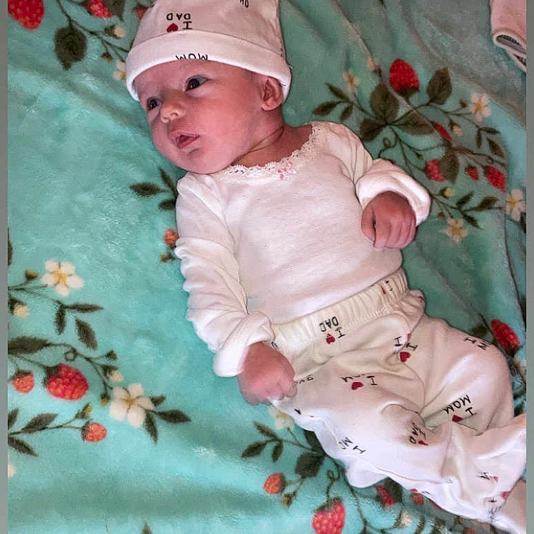 Brooklynn is registered to the contest to win money with this photo: baby, infant, child, portrait, lying_down, blanket, strawberry_pattern, floral_pattern, pink_hat, pajamas, long_sleeves, clothing, face, eyes, nose, mouth, indoor, bed, text_on_clothing, cozy