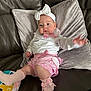 baby, infant, child, pink_clothing, white_headband, socks, bows, pillow, leather_couch, toy, reaching_hand, cute, indoors, soft_texture, playful, young_child, person, seated, comfortable, casual