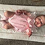baby, infant, pink_dress, socks, changing_mat, carpet, lying_down, smiling, face, skin, cute, child, young, indoors, soft_lighting, comfortable, adorable, person, human, closeup