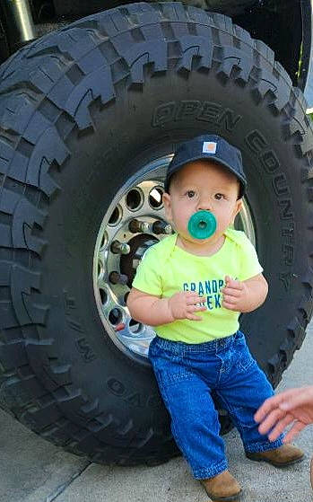 Winston is registered to the contest to win money with this photo: alloy_wheel, automotive_design, automotive_exterior, automotive_tire, automotive_wheel_system, baby_toddler_clothing, bumper, fender, hat, headwear, hubcap, motor_vehicle, person, plant, rim, synthetic_rubber, tire, tire_care, toddler, tread