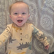 Taryn joined the competition — help win amazing prizes! baby, blanket, blue_eyes, casual_clothing, child, cozy, cute, dinosaur_onesie, face, hands, happy, indoors, infant, light_hair, lying_down, patterned_blanket, playful, smiling, soft_texture, toddler