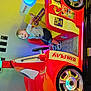 toddler, child, arcade, racing_car, smiling, toy_car, indoor, colorful, playful, happy, shorts, tshirt, footwear, hand, seat, wheel, game, entertainment, light, reflection