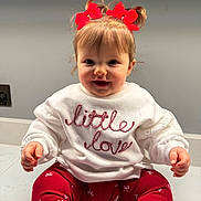 Dulcie is registered to the contest to win money with this photo: toddler, child, baby, red_bows, sweater, white_sweater, red_leggings, patterned_leggings, smiling, happy, sitting, indoor, cute, portrait, face, hands, hair, clothing, young_child, adorable