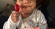 Autumn joined the competition — help win amazing prizes! baby, child, lollipop, onesie, cherry_pattern, hand, face, smile, indoor, person, cute, skin, holding, infant, clothing, expression, adult_hand, young_child, portrait, closeup