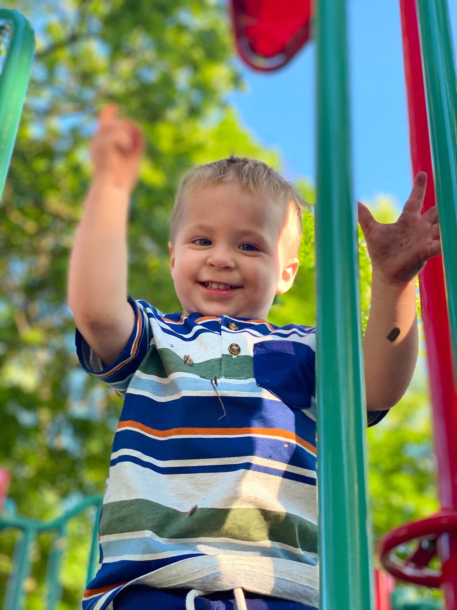 Michael is registered to the contest to win money with this photo: baby_toddler_clothing, child, fun, gesture, grass, happy, human_body, joy, leaf, leisure, people_in_nature, person, playground, public_space, red, smile, standing, summer, sunlight, swing