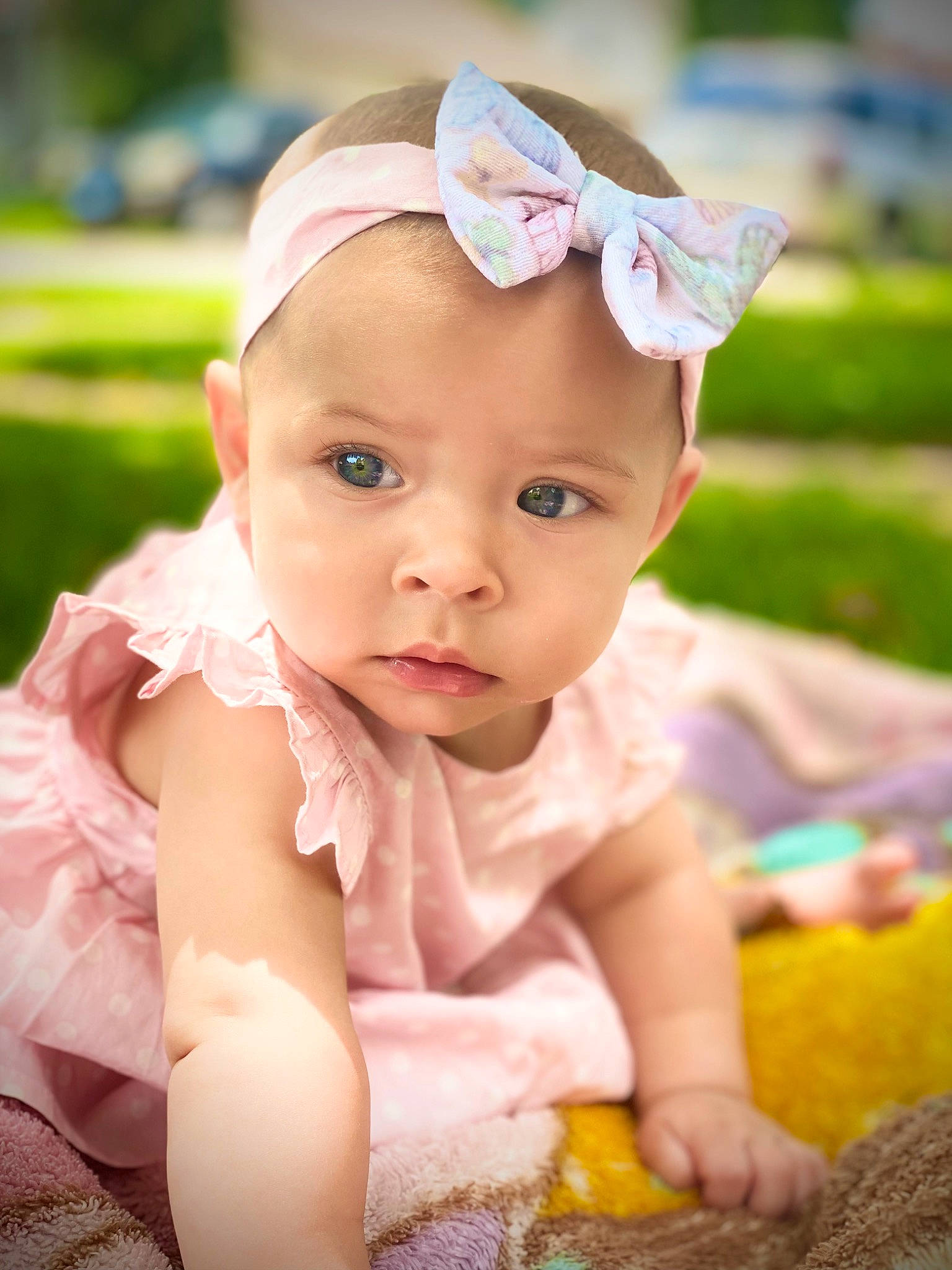 Avangeline is registered to the contest to win money with this photo: baby, baby_toddler_clothing, cheek, child, dress, face, fashion_accessory, fun, grass, happy, headband, headpiece, headwear, leisure, person, petal, pink, recreation, sitting, skin