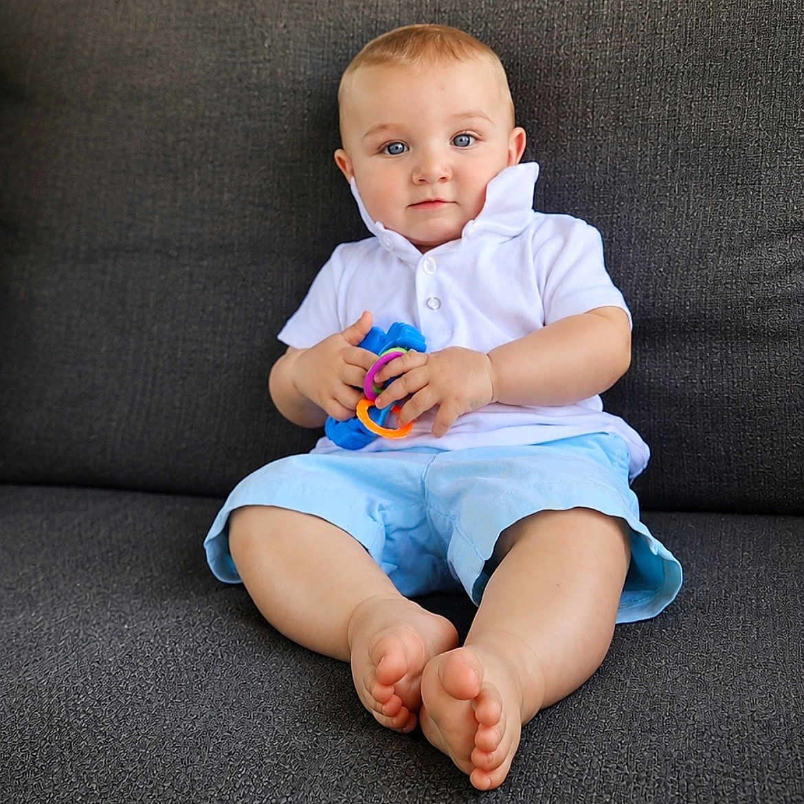 Owen joined the competition — help win amazing prizes! baby, child, blue_eyes, white_shirt, light_blue_shorts, toys, colorful, sitting, couch, indoor, barefoot, cute, portrait, young_child, hands, feet, comfortable, expression, texture, clothing