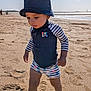 toddler, child, beach, sand, sunlight, hat, bucket_hat, swimsuit, striped_clothing, footprints, water, sea, outdoor, summer, walking, shoes, sunny, sky, person, baby_clothes
