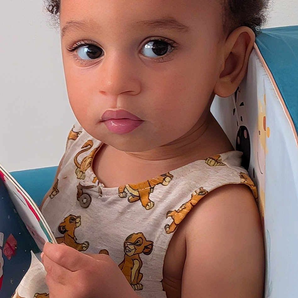 Alexis participe au concours pour gagner de l'argent avec cette photo : animal_print, blue_chair, book, child, clothing, curly_hair, cute, expression, face, indoor, innocent, looking, person, portrait, reading, seated, skin, small_hand, toddler, young_child