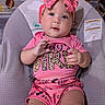 baby, child, infant, pink_bow, headband, pink_clothing, baby_seat, blanket, football_pattern, cute, smiling, hands, face, portrait, indoor, toddler, seat, apparel, patterned_clothing, happy