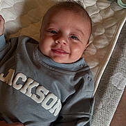 Jackson joined the competition — help win amazing prizes! baby, smiling, infant, quilted_mattress, gray_sweatshirt, text_on_clothing, hand, cute, happy, face, portrait, cozy, lying_down, indoor, child, human, sleeve, fabric, button, soft_lighting