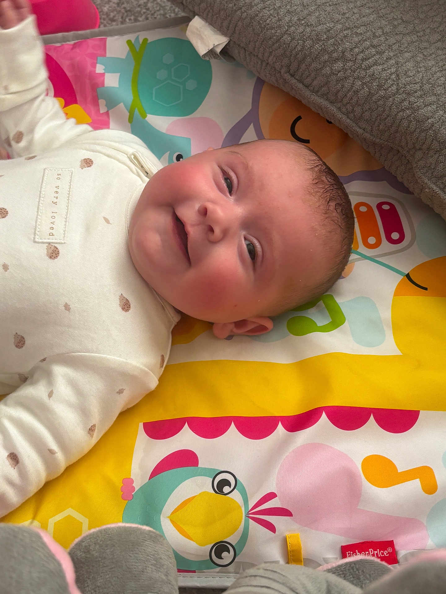 Riley is registered to the contest to win money with this photo: baby, infant, smiling, play_mat, colorful, blanket, cute, child, lying_down, indoors, clothing, patterned, face, head, happy, person, young_child, fisherprice, toy, soft_toys