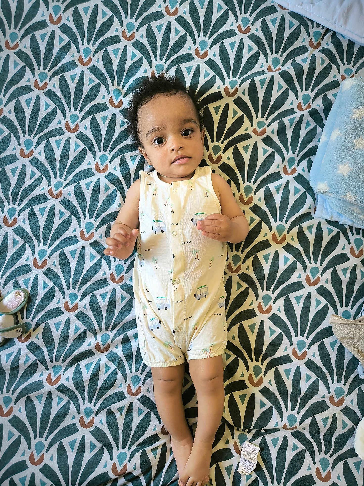 éden Naël a rejoint le concours — aidez-le/la à gagner de superbes lots ! baby, infant, child, romper, patterned_bedspread, lying_down, indoor, toy_shoe, blanket, curly_hair, looking_up, footwear, soft_toy, cute, small_hands, sleeping_area, fabric, expression, peaceful, comfortable