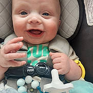 Gunnar is registered to the contest to win money with this photo: baby, smiling, car_seat, pacifier, toy, infant, child, happy, face, hand, close_up, seat_belt, clothing, beads, indoor, cute, skin, head, expression, sitting