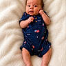 baby, infant, onesie, blue_clothing, american_flag, usa_text, blanket, white_blanket, cute, lying_down, small_hands, small_feet, portrait, indoor, soft_texture, child, newborn, skin, expression, face
